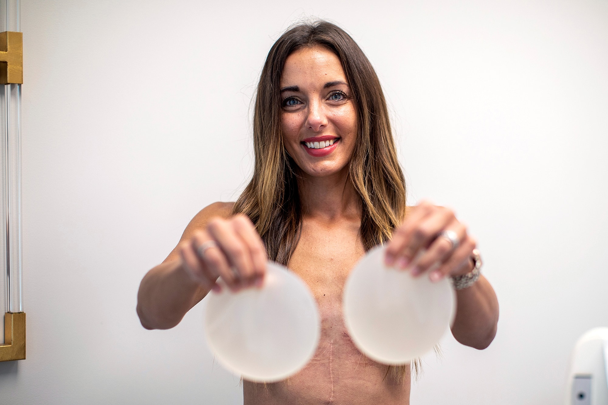 Woman holding breast implants, smiling confidently.